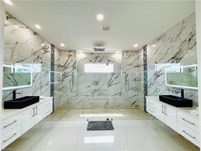 Bathroom with a marble finish shower, tile walls, two vanities, recessed lighting, and stone wall