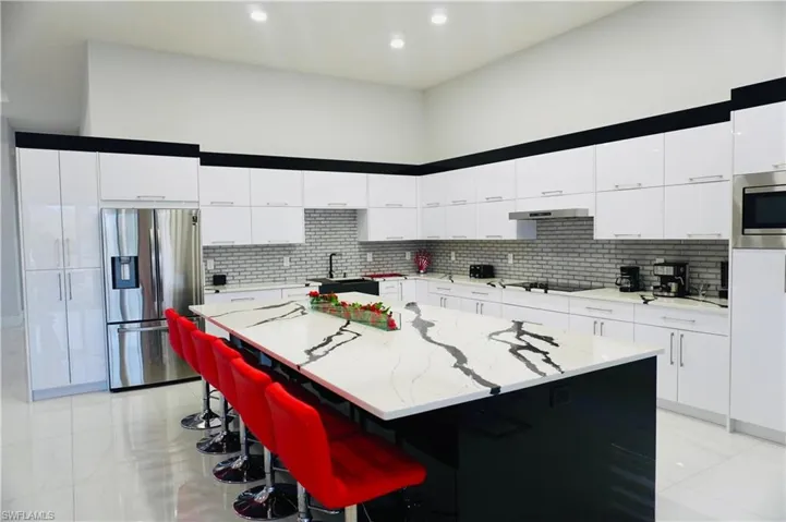 Two tone kitchen with stainless steel appliances, a center island, modern cabinets, light stone counters, and a kitchen bar