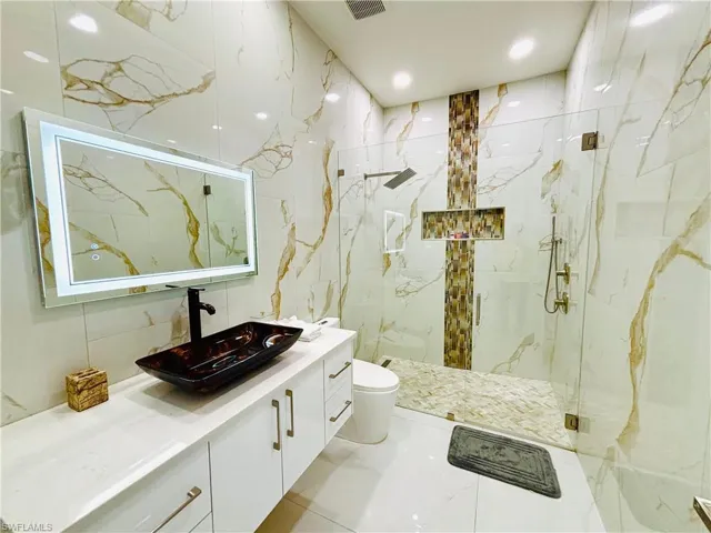 Full bath featuring vanity, a marble finish shower, and stone wall