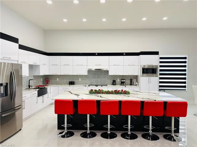 Kitchen featuring stainless steel appliances, a spacious island, modern cabinets, light stone countertops, and two tone color scheme