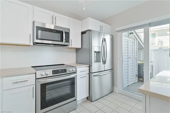 Kitchen with appliances with stainless steel finishes, white cabinetry, light stone countertops, light tile patterned floors, and decorative backsplash