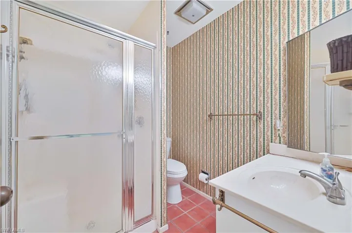 Bathroom with vanity, light tile patterned floors, wallpapered walls, and a shower stall