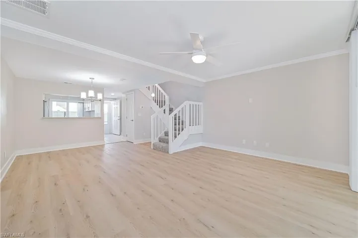 Unfurnished living room with stairway, light wood-style floors, a ceiling fan, ornamental molding, and a chandelier