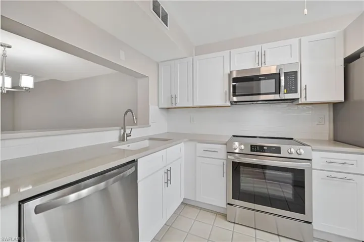 Kitchen with stainless steel appliances, white cabinets, light stone countertops, and pendant lighting