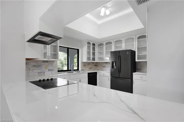 Kitchen with black appliances, white cabinets, light stone counters, and glass insert cabinets