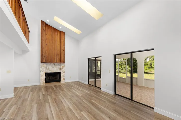 Unfurnished living room with high vaulted ceiling, light wood-type flooring, a skylight, a fireplace, and recessed lighting