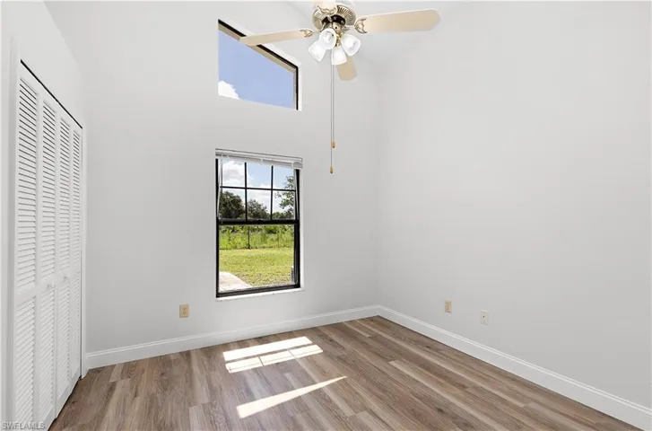 Unfurnished bedroom featuring wood finished floors, a closet, a towering ceiling, and a ceiling fan