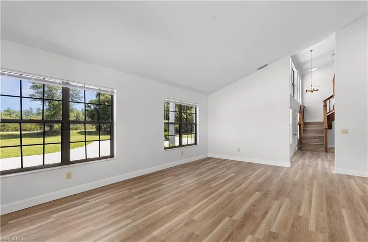 Spare room with stairway, light wood-style flooring, high vaulted ceiling, and a chandelier
