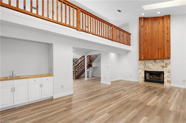 Unfurnished living room featuring stairs, recessed lighting, a high ceiling, a stone fireplace, and light wood-type flooring