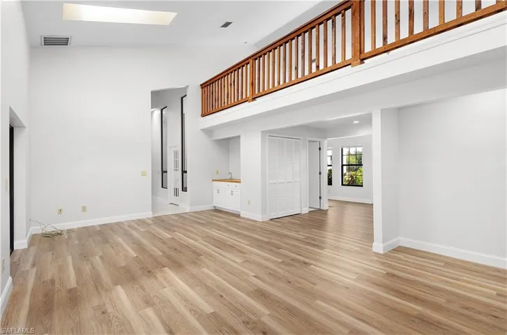Unfurnished living room with high vaulted ceiling, light wood-style flooring, and a skylight