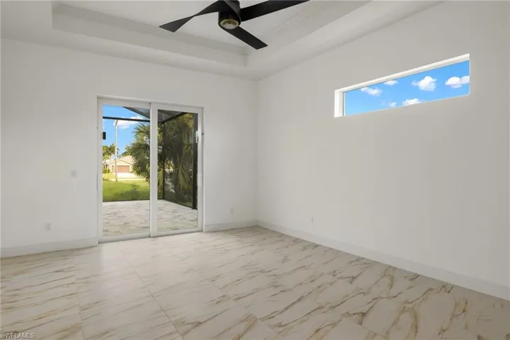 Unfurnished room with a tray ceiling, a ceiling fan, crown molding, and light marble finish flooring