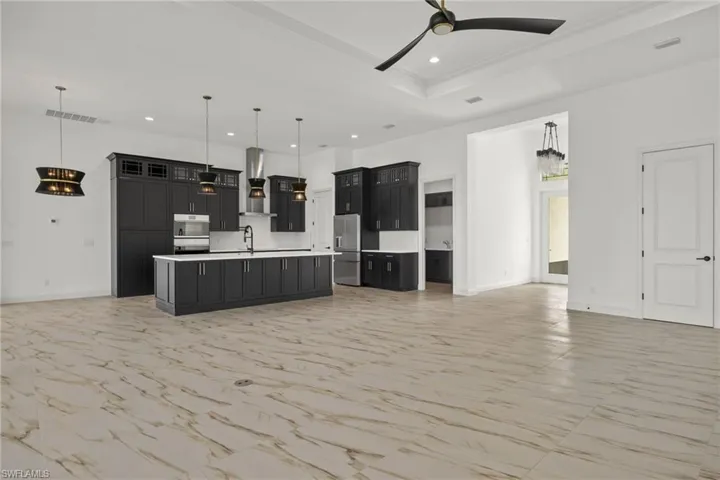 Kitchen featuring open floor plan, light countertops, glass insert cabinets, dark cabinetry, and wall chimney exhaust hood