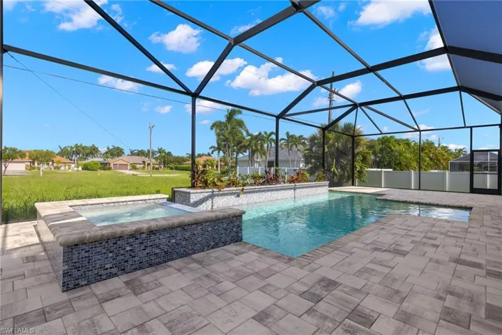 View of pool with a sunroom, glass enclosure, a pool with connected hot tub, a patio area, and a yard