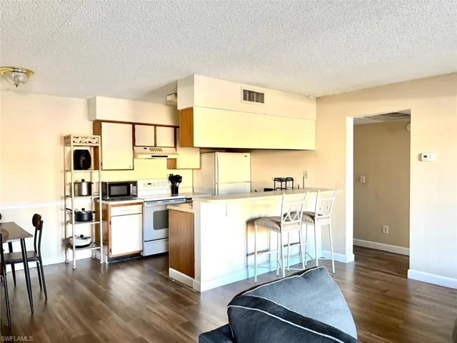 Kitchen with light countertops, brown cabinets, white appliances, a breakfast bar, and a textured ceiling