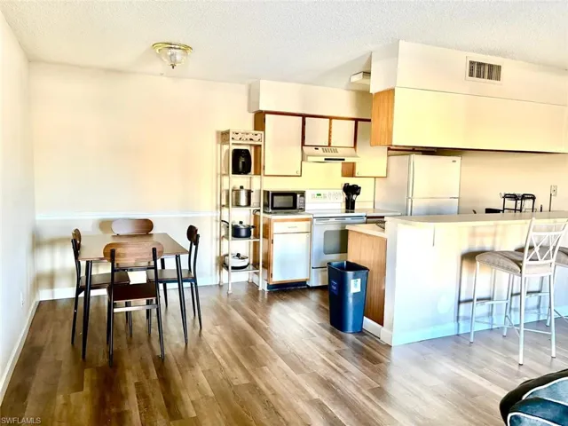 Kitchen featuring light countertops, a textured ceiling, white appliances, a kitchen bar, and under cabinet range hood