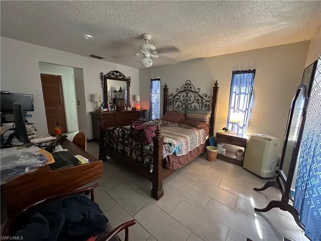 Bedroom featuring light tile floors, ceiling fan, a textured ceiling, and multiple windows