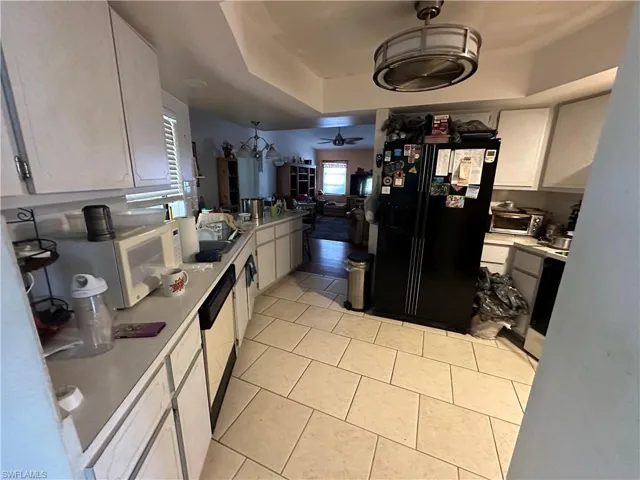 Kitchen with light tile flooring, black fridge, ceiling fan, a tray ceiling, and white cabinets