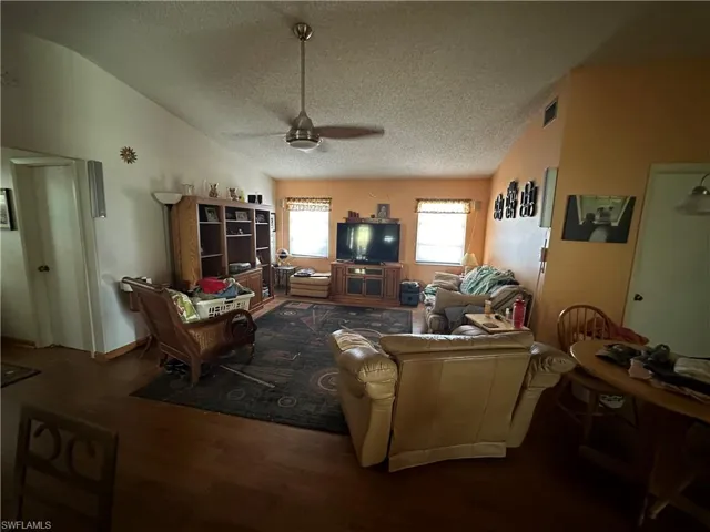 Living room with wood-type flooring, ceiling fan, a textured ceiling, and lofted ceiling