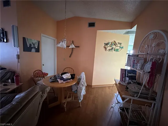 Dining room with vaulted ceiling, hardwood / wood-style flooring, and a textured ceiling