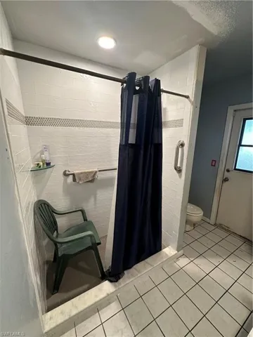 Bathroom featuring a shower with curtain, toilet, and tile floors