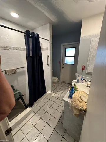 Bathroom featuring a shower with shower curtain, a textured ceiling, tile floors, sink, and toilet