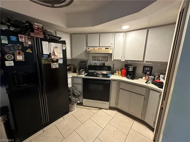 Kitchen featuring gas range gas stove, a tray ceiling, light tile floors, and black fridge with ice dispenser