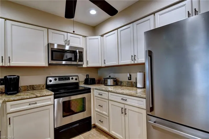 Kitchen with appliances with stainless steel finishes, light tile patterned floors, ceiling fan, and light stone counters