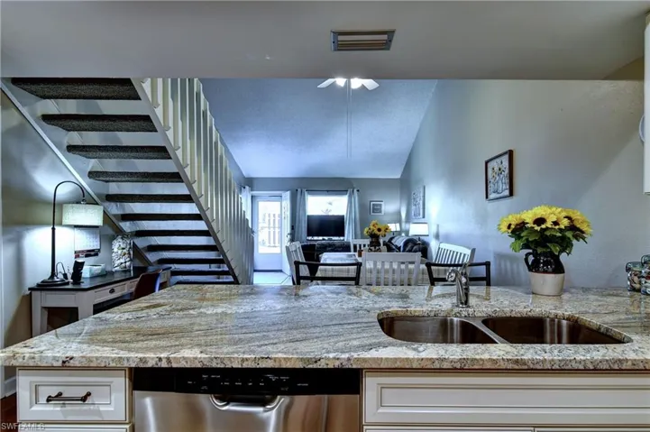 Kitchen with white cabinetry, ceiling fan, stainless steel dishwasher, light stone countertops, and sink