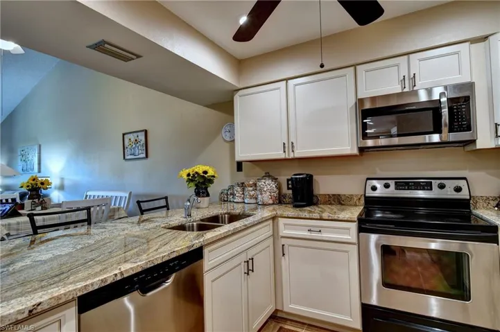 Kitchen with white cabinetry, ceiling fan, stainless steel appliances, sink, and light stone counters