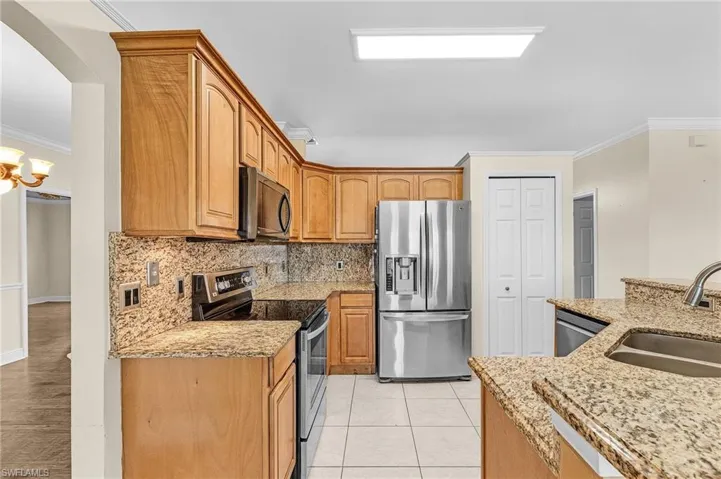 Kitchen with appliances with stainless steel finishes, a sink, ornamental molding, decorative backsplash, and light stone counters