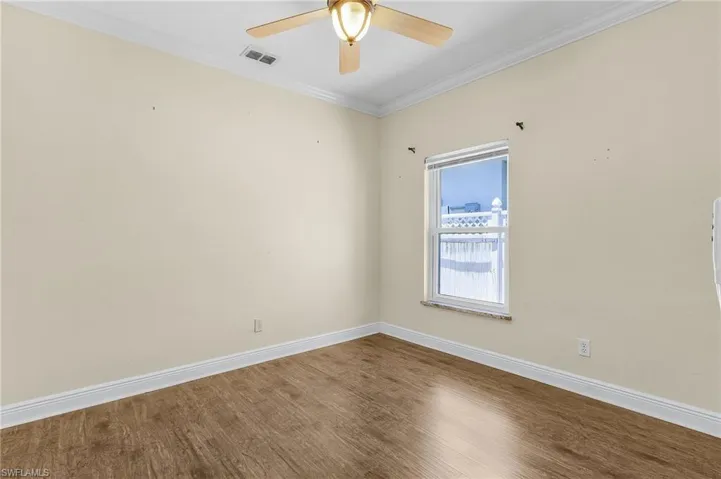 Empty room with wood finished floors, baseboards, ceiling fan, and ornamental molding