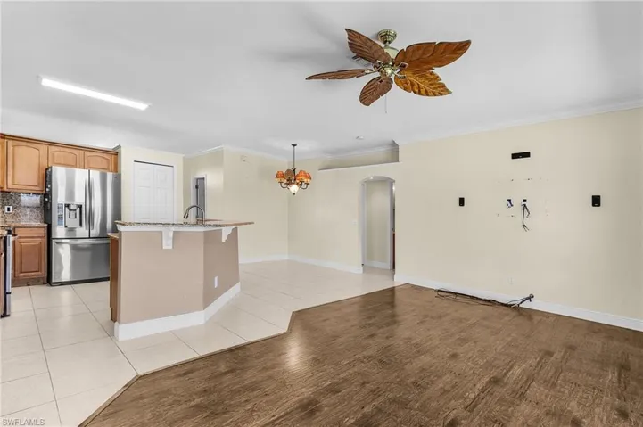 Kitchen with stainless steel refrigerator with ice dispenser, ceiling fan, arched walkways, a center island with sink, and ornamental molding