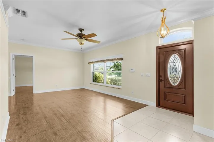 Foyer entrance with ornamental molding, a ceiling fan, light wood-type flooring, and baseboards