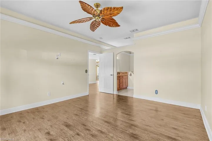 Empty room featuring arched walkways, a ceiling fan, light wood-type flooring, baseboards, and crown molding