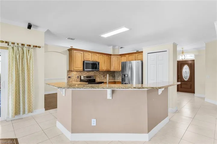 Kitchen featuring stainless steel appliances, light tile patterned floors, a kitchen bar, light stone counters, and crown molding