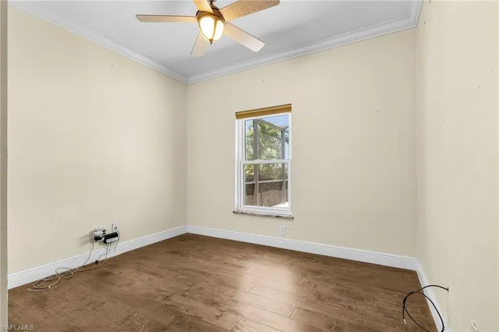 Empty room featuring crown molding, baseboards, wood finished floors, and ceiling fan