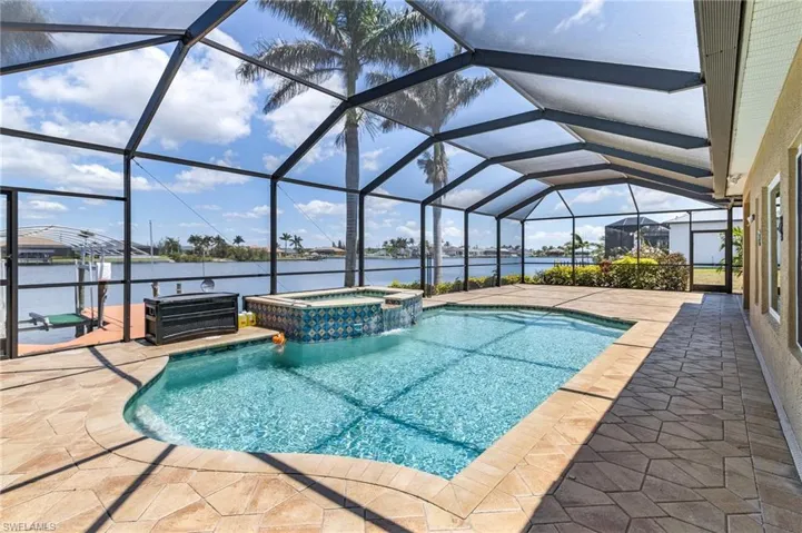 View of swimming pool featuring a water view, a patio area, a pool with connected hot tub, and a lanai