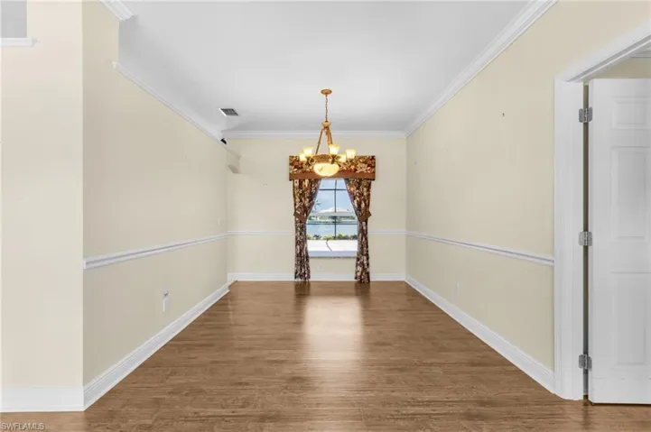 Unfurnished dining area featuring a chandelier, crown molding, wood finished floors, and baseboards