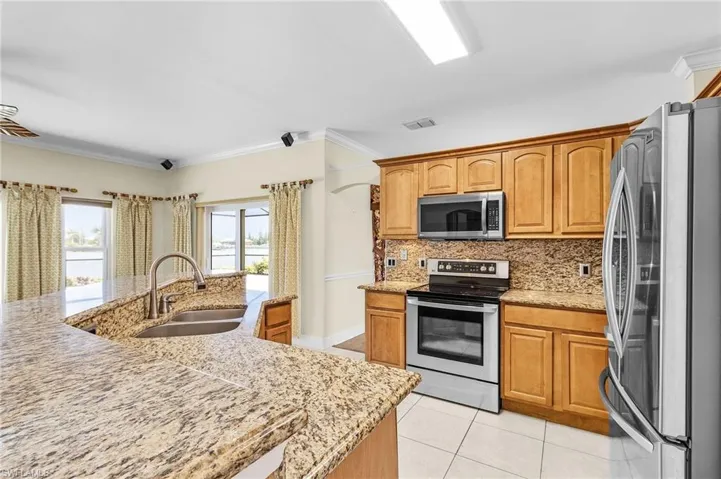 Kitchen featuring appliances with stainless steel finishes, a sink, light tile patterned floors, tasteful backsplash, and crown molding