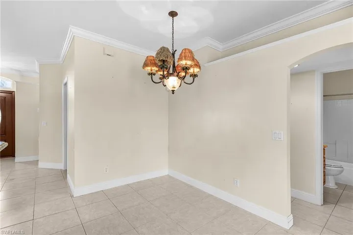 Unfurnished room featuring arched walkways, light tile patterned flooring, crown molding, a chandelier, and baseboards