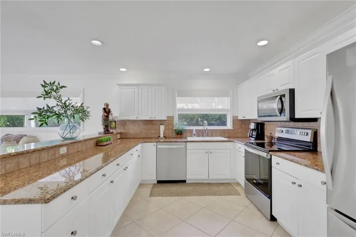 Kitchen featuring stainless steel appliances, light stone counters, white cabinets, ornamental molding, and recessed lighting