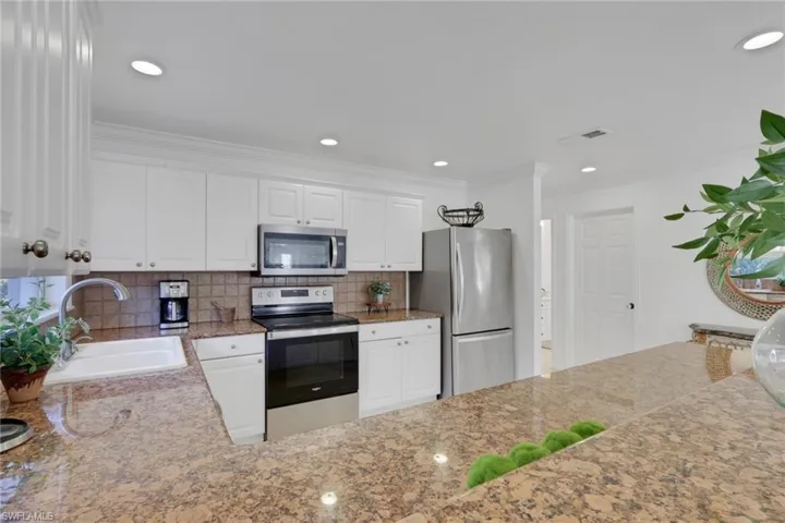 Kitchen featuring stainless steel appliances, white cabinetry, light stone countertops, decorative backsplash, and recessed lighting