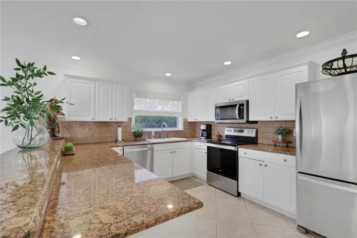 Kitchen featuring stainless steel appliances, white cabinetry, light stone counters, light tile patterned floors, and backsplash