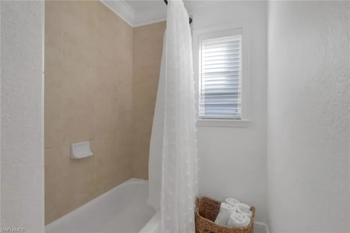 Bathroom with shower / bath combo, ornamental molding, and a textured wall