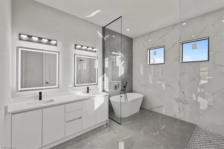 Full bath featuring a marble finish shower, double vanity, light marble finish floors, a freestanding tub, and recessed lighting