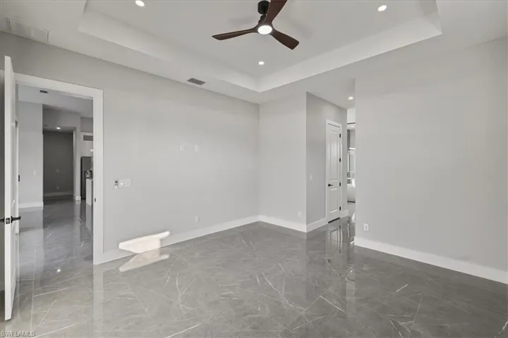 Unfurnished room with a raised ceiling, dark marble finish floors, recessed lighting, and ceiling fan