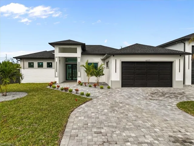 Prairie-style house with a front lawn, stucco siding, a shingled roof, and decorative driveway