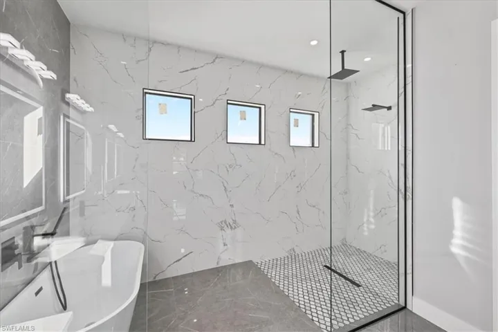 Bathroom featuring a marble finish shower, marble tiled floors, stone wall, and a soaking tub