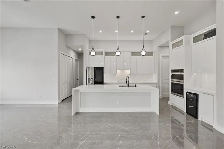 Kitchen with glass insert cabinets, white cabinets, light marble finish flooring, a large island, and light stone countertops