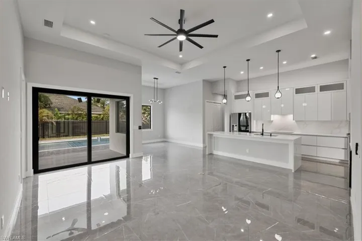 Living room with a tray ceiling, light marble finish floors, ceiling fan, recessed lighting, and a high ceiling
